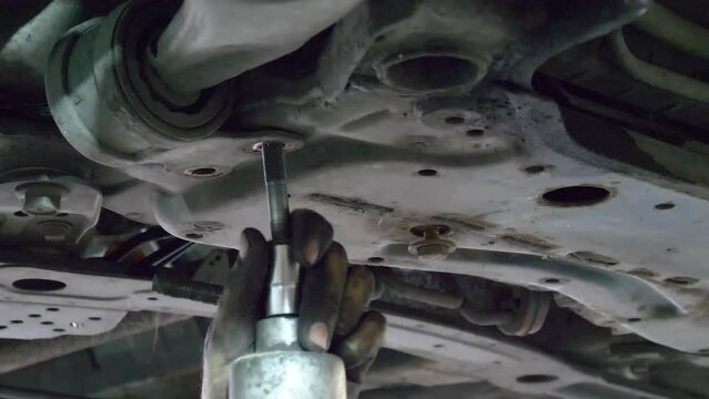 Close up unscrewing car bolts. Dirty hands of an auto mechanic unscrew bolts on bottom of car, close-up. Male mechanic unscrew car detail of running gear of car. Car suspension repair.