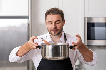 Man cooking at kitchen. Handsome man preparing delicious meal in modepn kitchen. Male chef cooking in kitchen. Millennial man preparing a healthy meal on kitchen home background. Kitchens utensils.