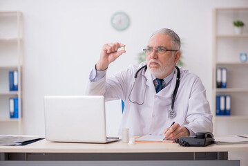 Old male doctor suggesting pills in the clinic