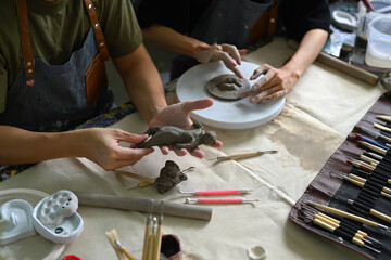 Craftspeople wearing aprons working with raw clay, shaping and decorating pottery in workshop