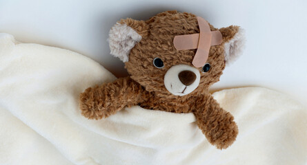 Sick teddy bear toy with patch in on head lying in bed