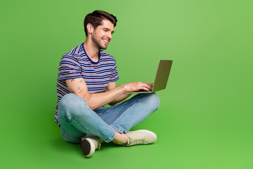 Full length photo of cool funky man dressed striped t-shirt working modern gadget empty space isolated green color background