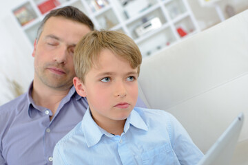 Obraz premium Boy on tablet looking pensive while father sleeps