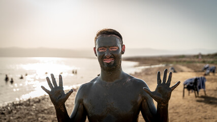 Man covered in mud at dead sea in jordan at sunset 