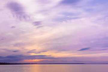 Naklejka na ściany i meble Colorful sky background on sunset or sunrise, purple pastel color clouds and surface water on lake. Aesthetic view nature abstract cloudscape, natural blue pink purple shades and skyline water