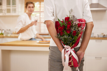 young gay couple looking at boyfriend and holding bouquet of roses behind his back for surprise in...