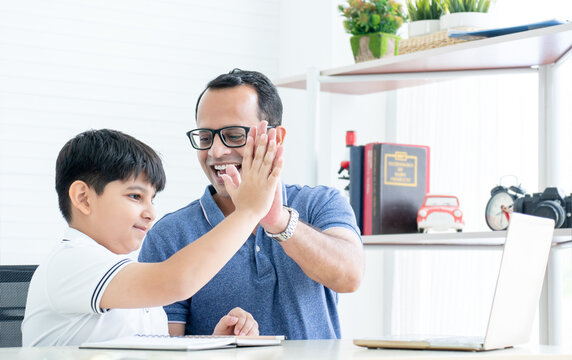 Indian Family, Happy Handsome Little Child Boy And Father Doing High Five While Online Studying With Laptop At Home. Dad Teaching, Helping Son Doing Homework. Online Learning. Education Concept