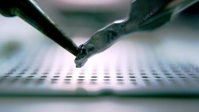 Soldering device melting hard metal from special stick on panel with small holes. Light exposes process of melting metal closeup