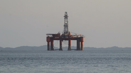 Offshore oil platform drilling site or oil rig project seen far in the middle of the sea.