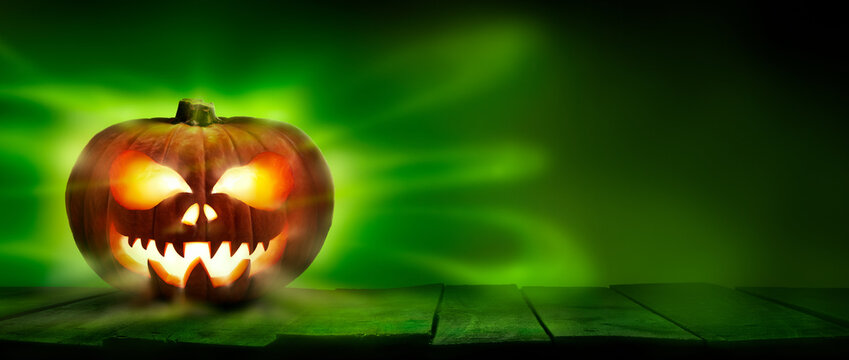 A spooky halloween pumpkin, Jack O Lantern, with an evil spinning green aura glow on a wooden table against a dark background.