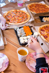 Flat lay of a table with Group of young friends eating pizza and sushi, rolls in living-room. Soft focus, 6 October 2022. Russia. High quality photo