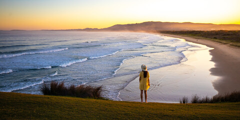 Beautiful girl in yellow dress on green hill admires colorful sunset on the coast. Look At Me Now...