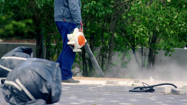 Employee dressed in uniform cleans public floor. Man uses vacuum cleaner to remove dust and debris from sidewalks of city
