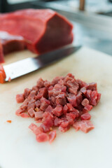 Tonno crudo tagliato a pezzetti su tagliere bianco per preparazione di una tartare con coltello sullo sfondo e trancio di tonno