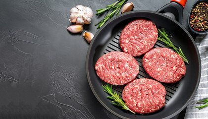 raw burgers - cutlets from organic beef meat with garlic and rosemary in a frying pan on black...