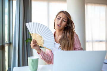 A young woman sweats profusely while working on her laptop in an overheated home office. With no...