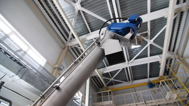 Metal pipe lifted up to ceiling in spacious production workshop. Ventilation system made of hot-dip galvanized sheet in production shop