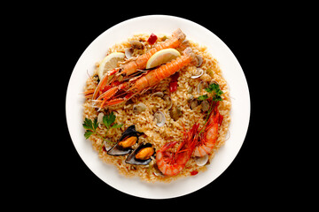 Seafood paella with seafood. In white plate on black background