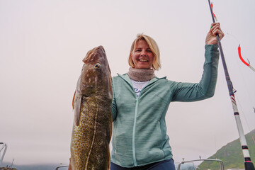 Happy young fisherwoman holding big arctic cod. Norway happy fishing. Happy woman with cod fish in...