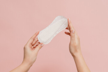 Sanitary napkin in woman's hand on pink background