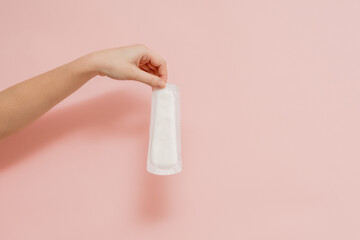 Sanitary pad in woman's hand on pink background