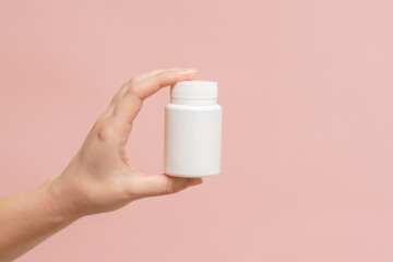 White bottle (plastic tube) in hand on pink background. Packaging for vitamins, pill or capsule, or supplement. Mockup for product branding