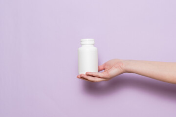 White plastic bottle in female hand. Packaging for pills, capsules or supplements.