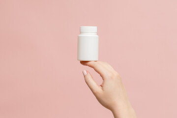 Plastic bottle (tube) in hand on pink background. Packaging for vitamins, tablets or capsule, or supplement