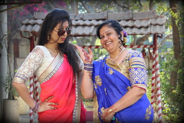bonding between mother and daughter - daughter in law. Two ladies in Indian saari and traditional attire posing in a style. Happy mother - daughter in festive look with Mehendi applied on their hand 