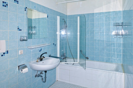 Unrenovated bathroom from the 1970s with the original blue tiles, seventies style. Outdated, neglected and grimy bath in an apartment for rent.