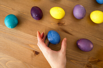 Female hand holding colorful Easter eggs on wooden background. Top view.
