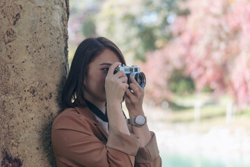 Asian Women with vintage film camera take a photo. Smiling female photographer look at photo from professional camera outdoor. Young woman shooting photo in green nature park. Beautiful woman hobby