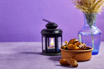 pottery bowl of pitted dates with arabic lantern and reeds plant vase isolated on purple...