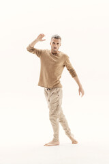 A young man in a beige jumper and cargo pants on a white background.