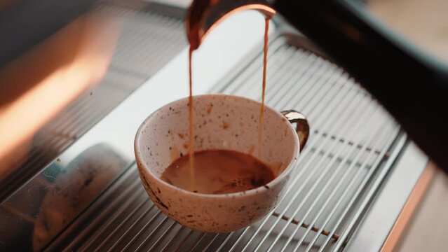 Closeup shot of espresso steam coffee machine start pouring fresh hot coffee into a white cup at morning cafe in slow motion