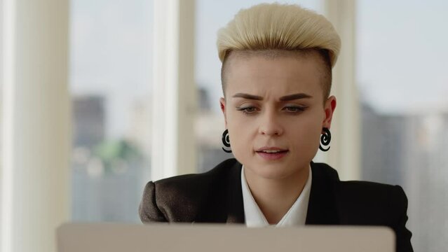 informal girl in a suit works in the office. The concept of working in a large office. Atractive girl with white hair work on laptop and type text, make internet research, and drink coffee because she