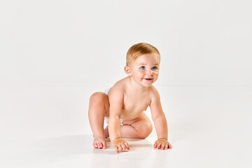 Cute, lovely little baby girl, toddler in diaper sitting on floor and starting crawling against...