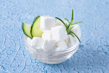 Feta cheese, cucumber and herbs in a bowl on blue background