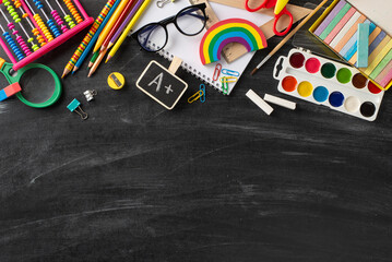 Elementary school assortment. Top view of color pencils, album, drawing paints, A+ grade, plasticine, chalk, ruler, clips, spectacles, magnifying glass, abacus on blackboard with room for text or ad - Powered by Adobe