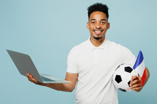 Young fun IT man fan wears basic t-shirt cheer up support football sport team hold French flag use work on laptop pc computer soccer ball watch tv live stream isolated on plain blue color background.