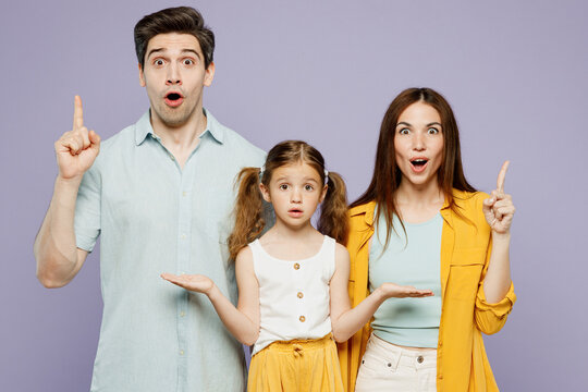 Young Happy Parents Mom Dad With Child Kid Daughter Girl 6 Years Old Wear Blue Yellow Casual Clothes Holding Index Finger Up With Great New Idea Isolated On Plain Purple Background Family Day Concept