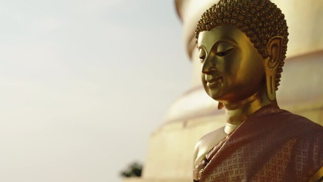 Zoom out camera moves with parallax effect from the face of golden sitting Buddha statue on the mountain of the temple complex with a Buddhist stupa. Sunrise wide angle shot