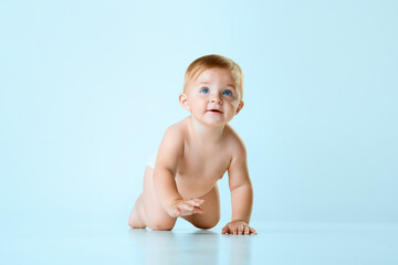 Little cute baby, child, toddler in diaper crawling on floor against light blue studio background. Blue eyes. Concept of childhood, newborn lifestyle, happiness, care. Copy space for ad - obrazy, fototapety, plakaty