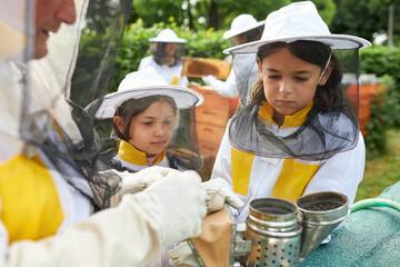 Senior male beekeeper teaching about smoker to girls - Powered by Adobe