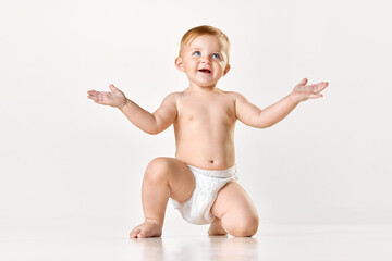 Adorable little baby, child in diaper calmly sitting and playing against white studio background....
