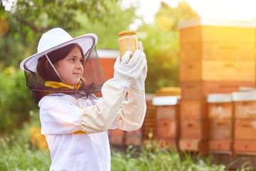 Girl as beekeeper holding glass of honey in front of beehives