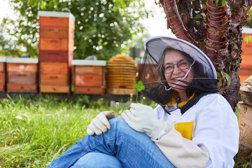 Happy senior female apiculturist sitting at apiary