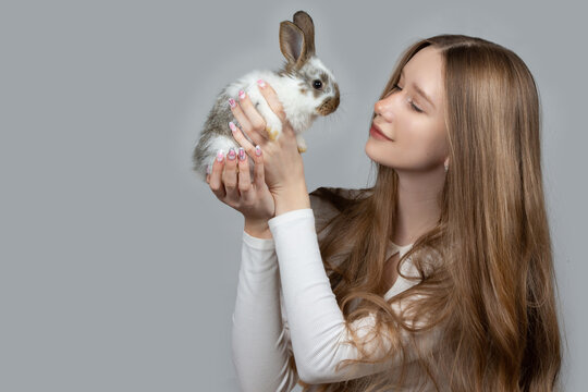 Happy young girl holding a white rabbit on a gray background