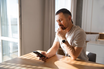 man  with mobile phone  reads messages or news sitting at the table at home. concept without...