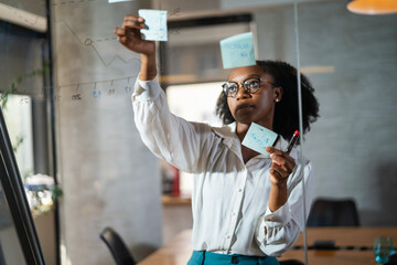 Businesswoman in conference room. Young African businesswoman making a business plan. Woman writing on the glass board in office..
